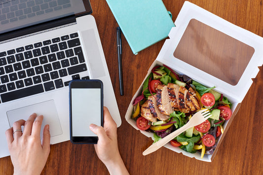 a person working on their computer with a salad sitting next to them