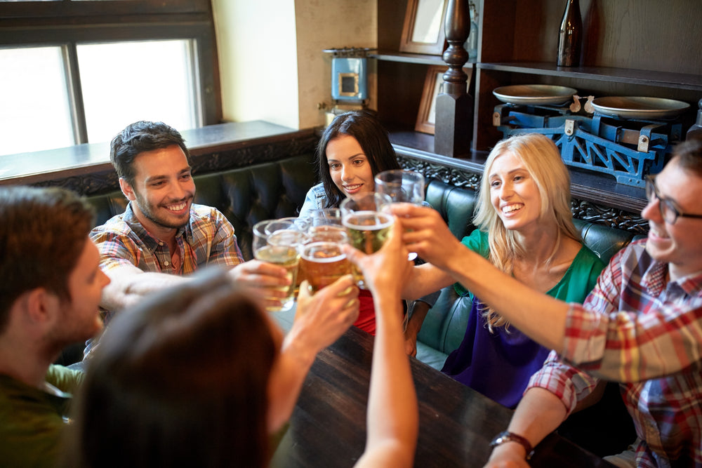 happy friends drinking beer and clinking their glasses at a bar