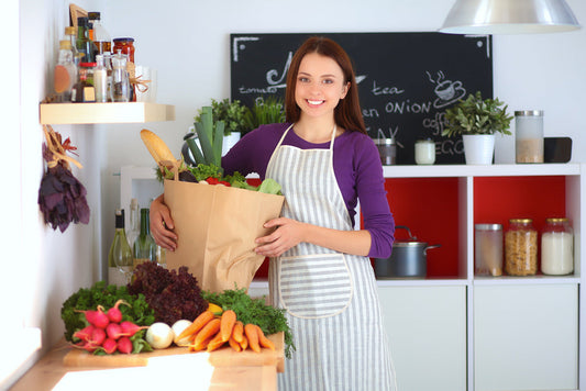 Young woman standing in kitchen holding grocery shopping bag with vegetables