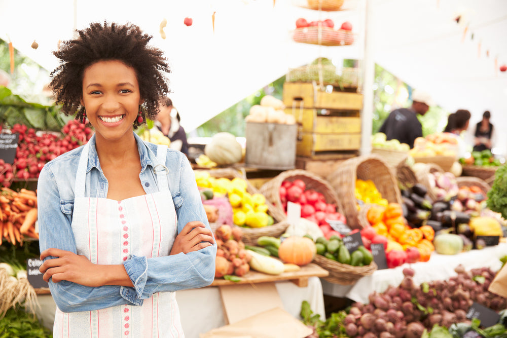 a woman staning by fruits an vegetables in a farmers market