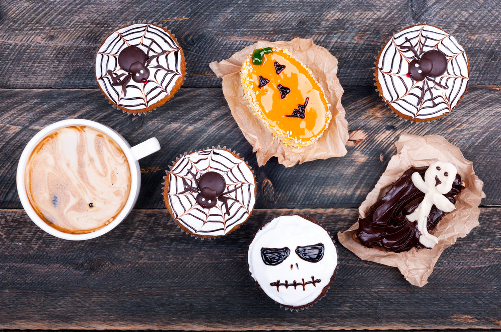 Pumpkin muffins with spiders, skull, ghost and cup of coffee set on rustic table for Halloween party food