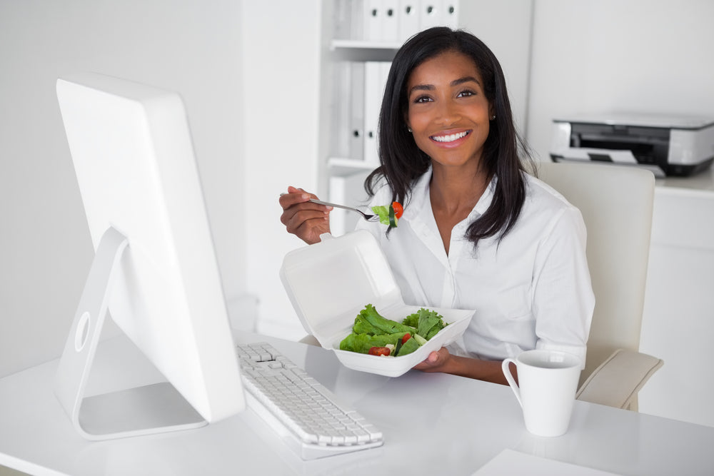 Smiling young businesswoman eats salad at her desk