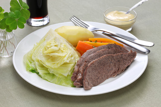 Corn beef &amp; cabbage with potatoes, carrots, mustard sauce; beer and shamrocks in background