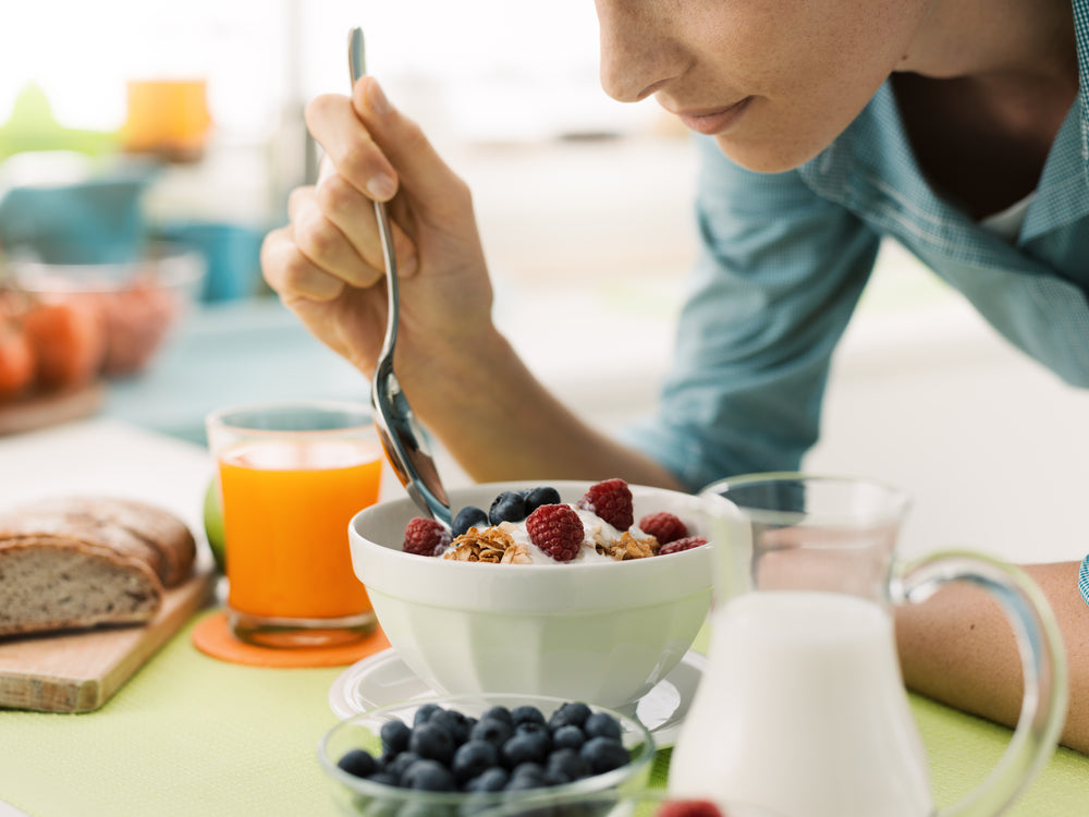 a woman eating a bowl of yogurt with fruits and nuts