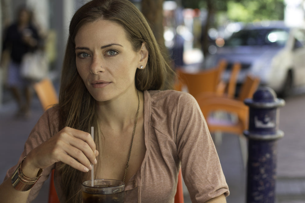 a woman staring at the camera with her fingers wrapped around a straw coming out of a drink